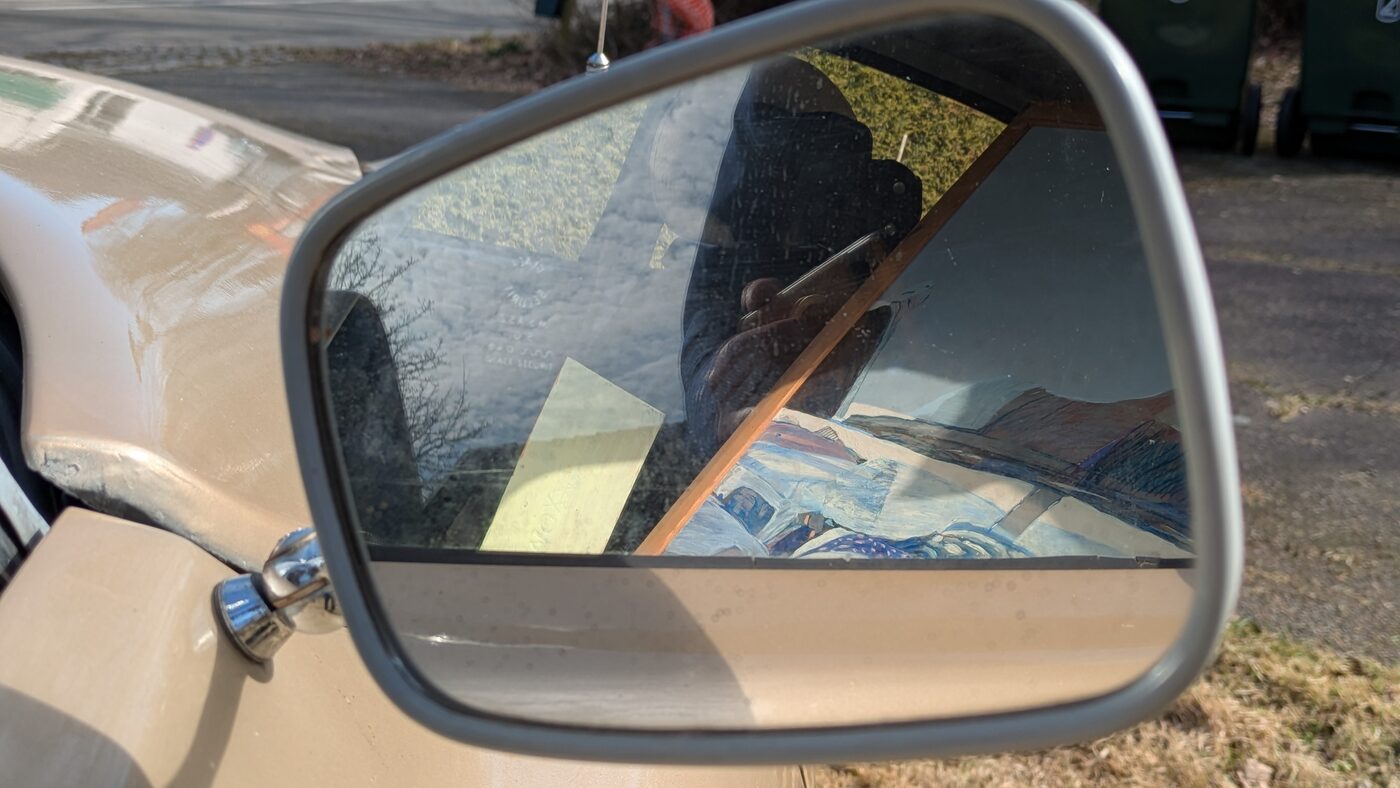 A painting reflected in the wing mirror of the car