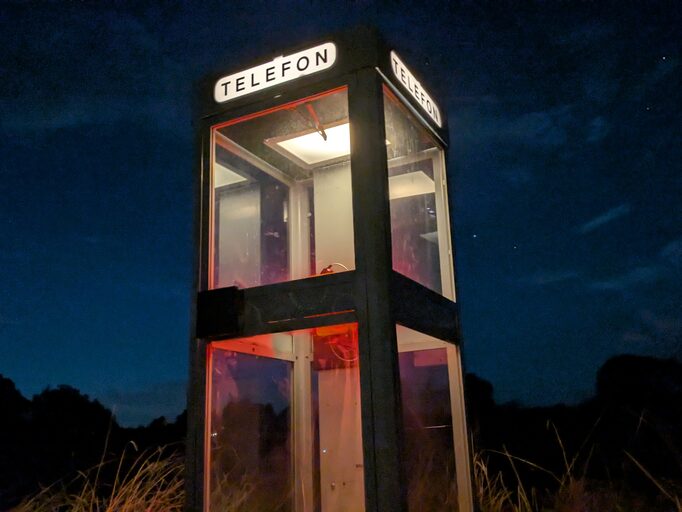 LINJEN, a phone booth lit against the night sky in a field